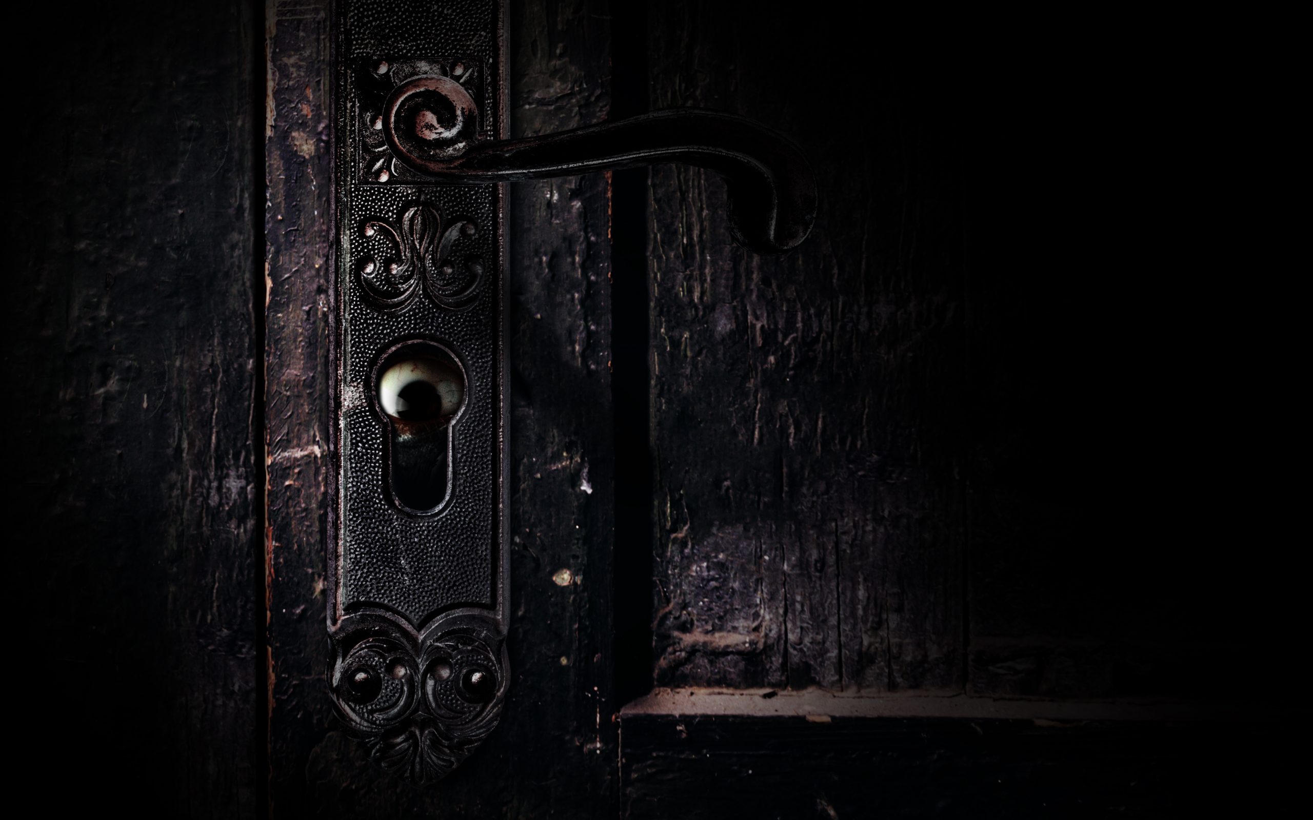 Photo of old obsoltete and shaded abandoned grungy door handle with horror scary eye peaking from keyhole.